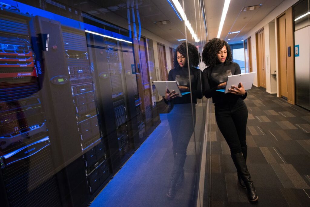 pexels photo 1181316 A woman using a laptop navigating a contemporary data center with mirrored servers.