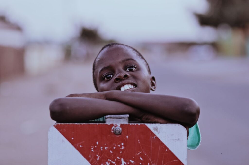 pexels photo 3116262 A cheerful young African boy leans on a barrier in Soshanguve, South Africa, smiling warmly at the camera.